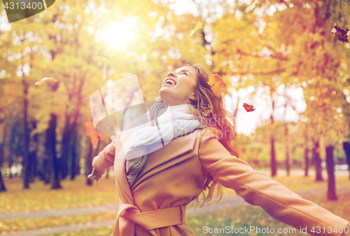 Image of happy woman having fun with leaves in autumn park