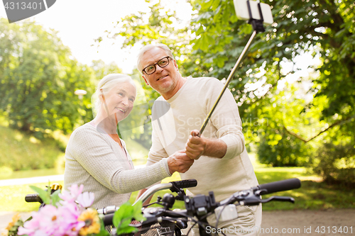 Image of senior couple with bicycles taking selfie at park