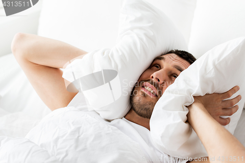 Image of man in bed with pillow suffering from noise