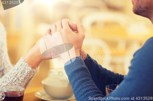Image of happy couple with tea holding hands at restaurant