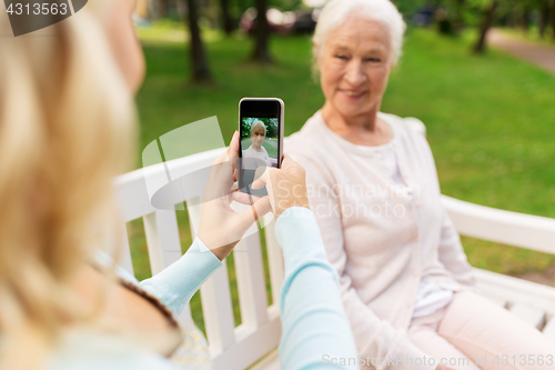 Image of daughter photographing senior mother by smartphone