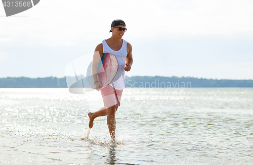 Image of happy young man with skimboard on summer beach