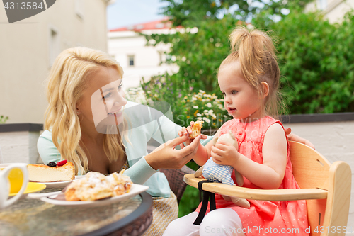 Image of happy mother feeding daughter with cake at cafe