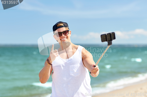 Image of man with smartphone selfie stick on summer beach
