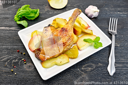 Image of Duck leg with apple and potatoes in plate on black board