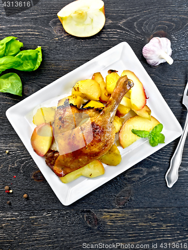 Image of Duck leg with apple and potatoes in plate on board top