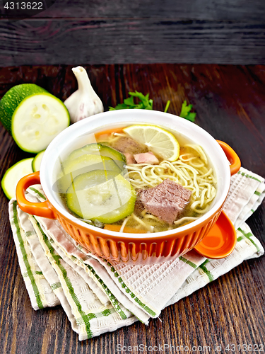 Image of Soup with zucchini and noodles in red bowl on towel