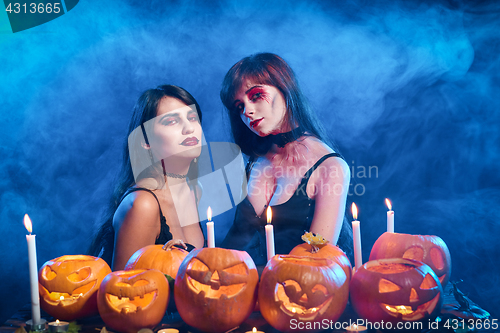 Image of Two beautiful sexy witches with Halloween pumpkins