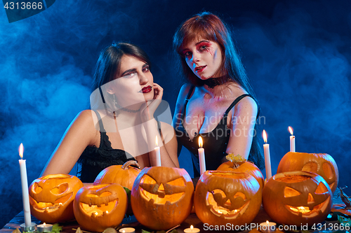 Image of Two beautiful sexy witches with Halloween pumpkins