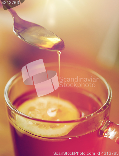 Image of close up of woman adding honey to tea with lemon