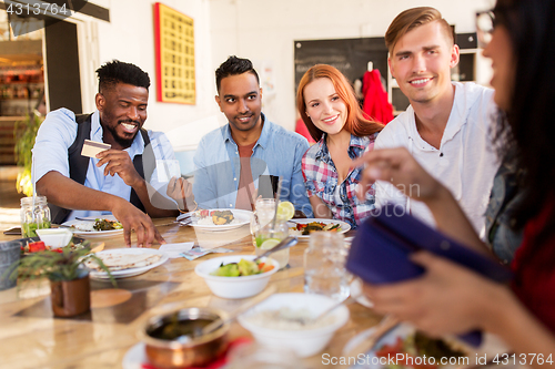 Image of happy friends with money paying bill at restaurant