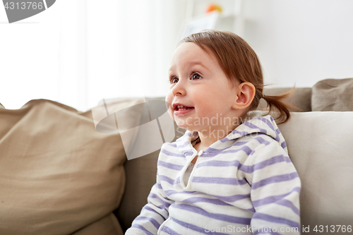 Image of happy smiling baby girl sitting on sofa at home