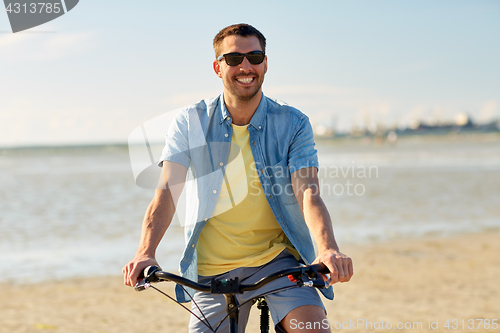 Image of happy man riding bicycle along summer beach