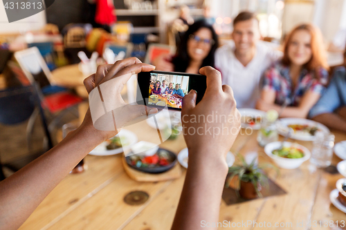 Image of friends taking picture by smartphone at restaurant