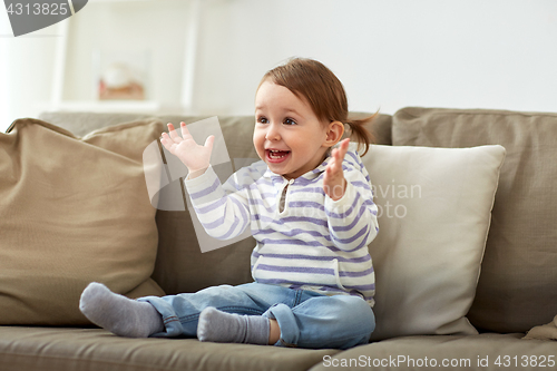 Image of happy smiling baby girl sitting on sofa at home