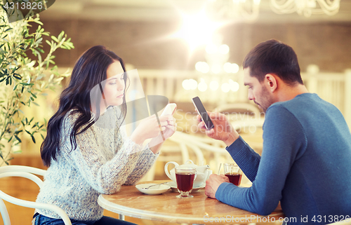 Image of couple with smartphones drinking tea at cafe