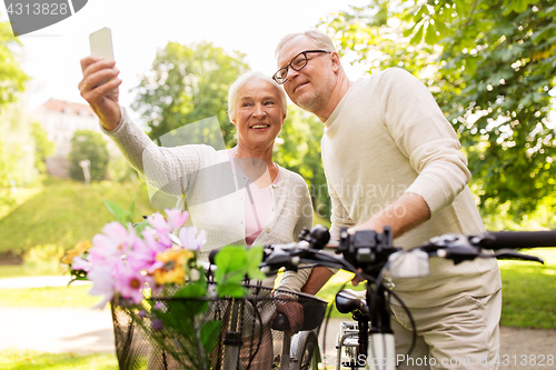 Image of senior couple with bicycles taking selfie at park