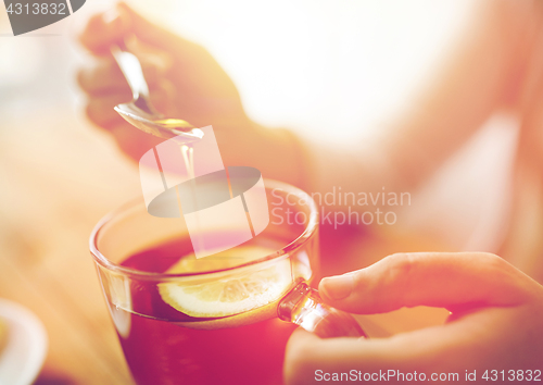 Image of close up of woman adding honey to tea with lemon