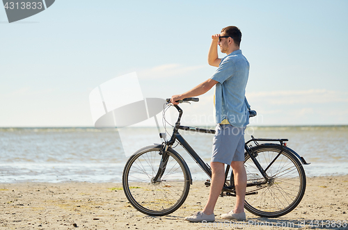 Image of happy young man with bicycle on beach 