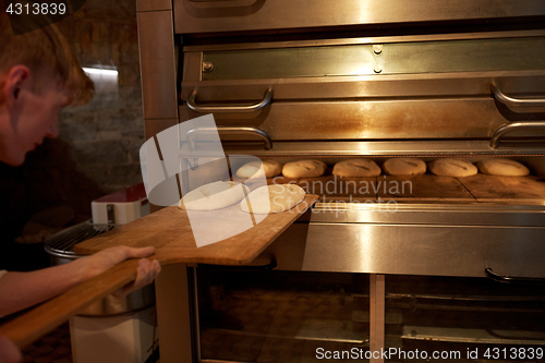 Image of baker putting dough into bread oven at bakery