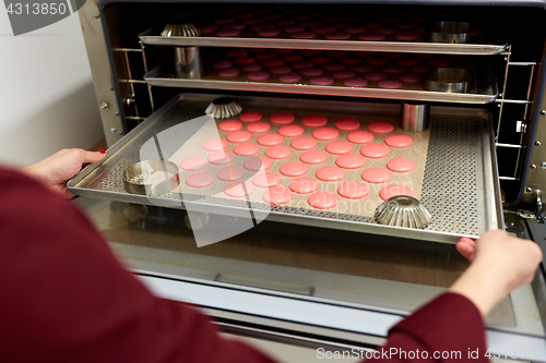 Image of chef with macarons on oven tray at confectionery