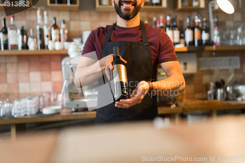 Image of happy man or bartender with bottle of wine at bar