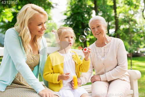Image of happy family blowing soap bubbles at park