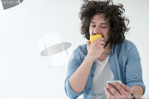 Image of young man eating apple and using a mobile phone  at home