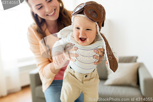 Image of happy mother with baby wearing pilot hat at home