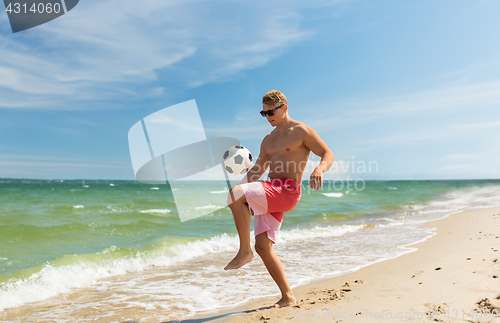 Image of young man with ball playing soccer on beach