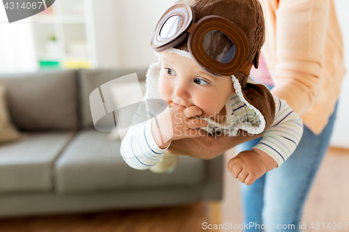 Image of happy mother with baby wearing pilot hat at home