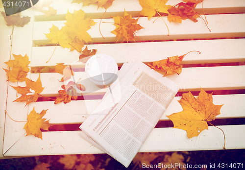 Image of newspaper and coffee cup on bench in autumn park