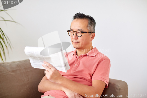 Image of happy man in glasses reading newspaper at home