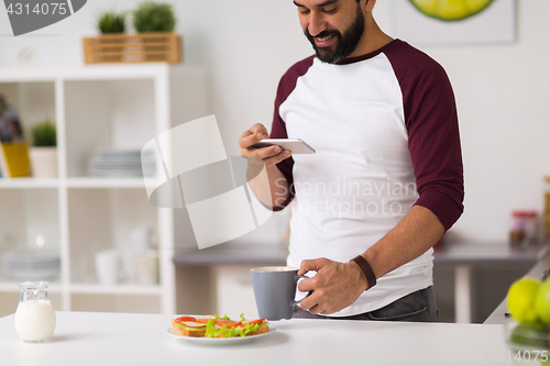 Image of man with smartphone and coffee eating at home