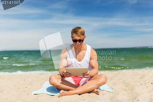 Image of happy smiling young man with tablet pc on beach
