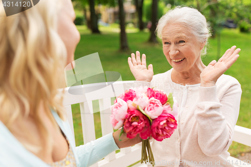 Image of daughter giving flowers to senior mother at park