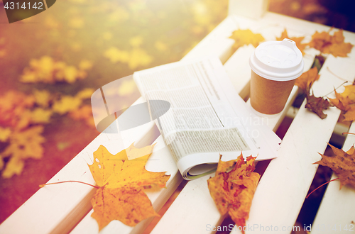 Image of newspaper and coffee cup on bench in autumn park