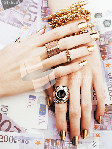 Image of hands of rich woman with golden manicure and many jewelry rings 