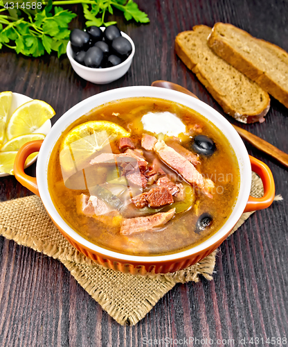 Image of Solyanka with lemon and spoon in bowl on dark board