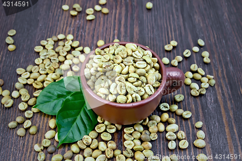 Image of Coffee green grain in cup with leaf on dark board