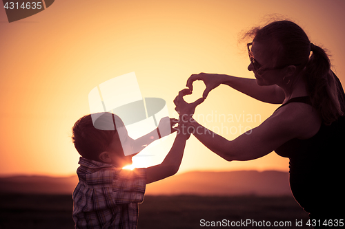 Image of Mother and son walking on the field at the sunset time.