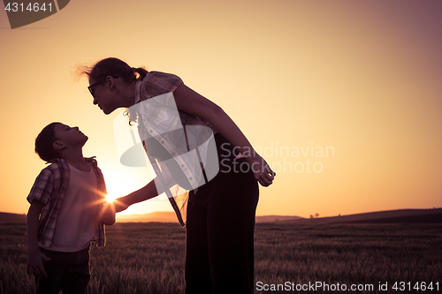 Image of Mother and son walking on the field at the sunset time.