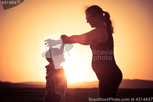 Image of Mother and son walking on the field at the sunset time.