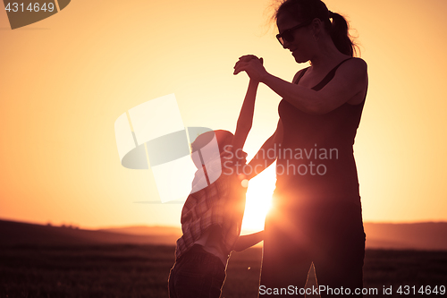 Image of Mother and son walking on the field at the sunset time.