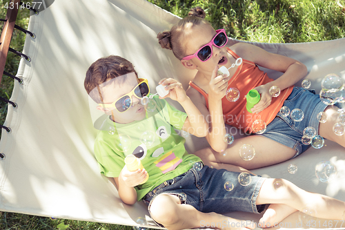 Image of Two happy children lie on a hammock and play with soap bubbles