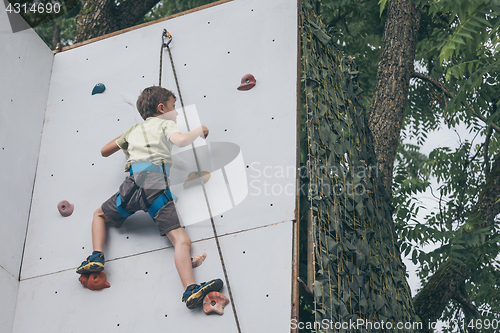 Image of little boy climbing a rock wall outdoor.