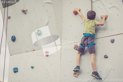 Image of little boy climbing a rock wall outdoor.