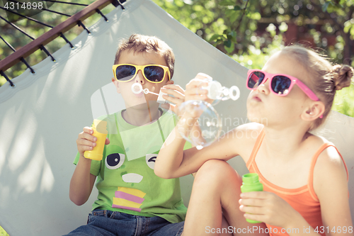 Image of Two happy children lie on a hammock and play with soap bubbles