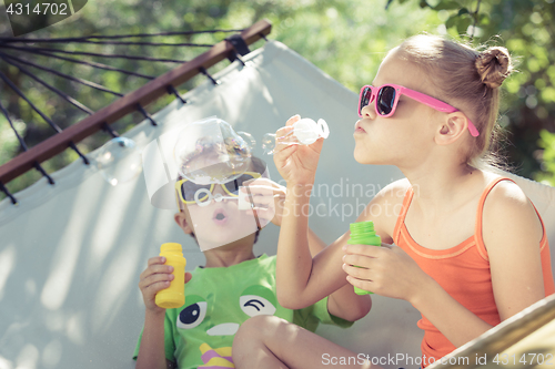 Image of Two happy children lie on a hammock and play with soap bubbles