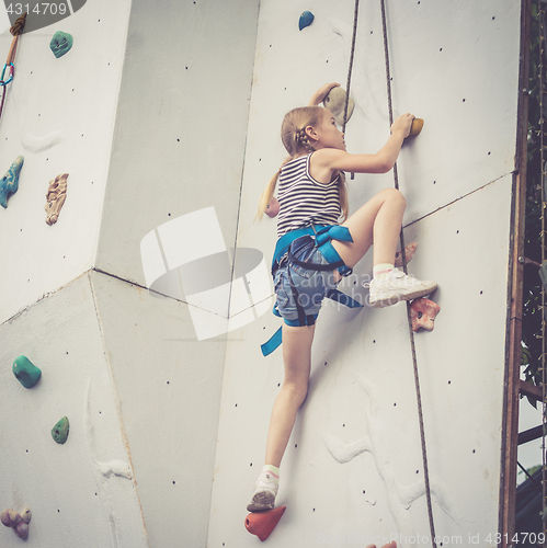 Image of little girl climbing a rock wall outdoor.